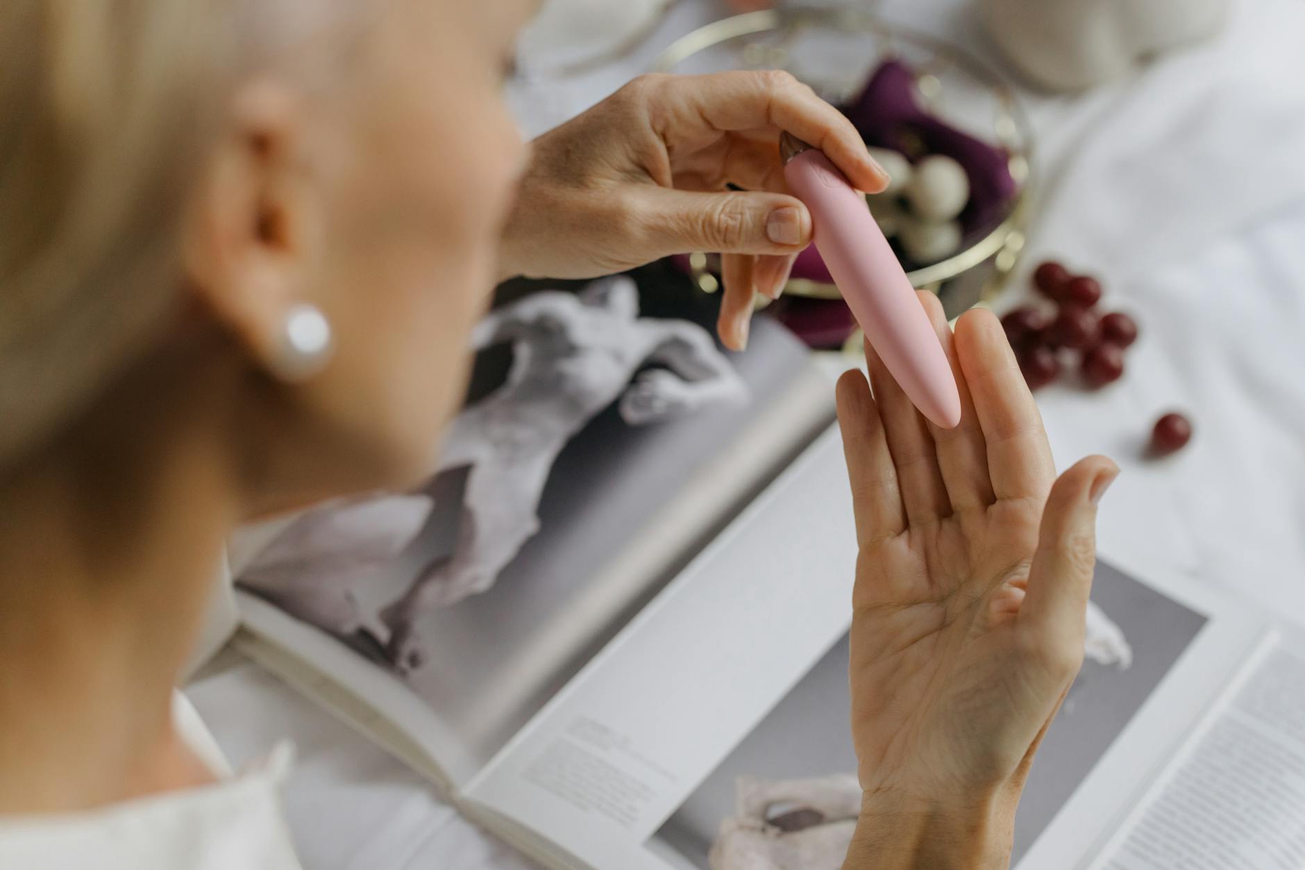 A woman holding blue and pink clitoral vibrators in a thoughtful, intentional pose